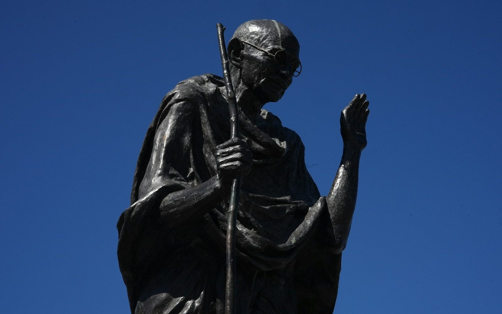 A statue of Mahatma Gandhi walking with his staff against a clear sky