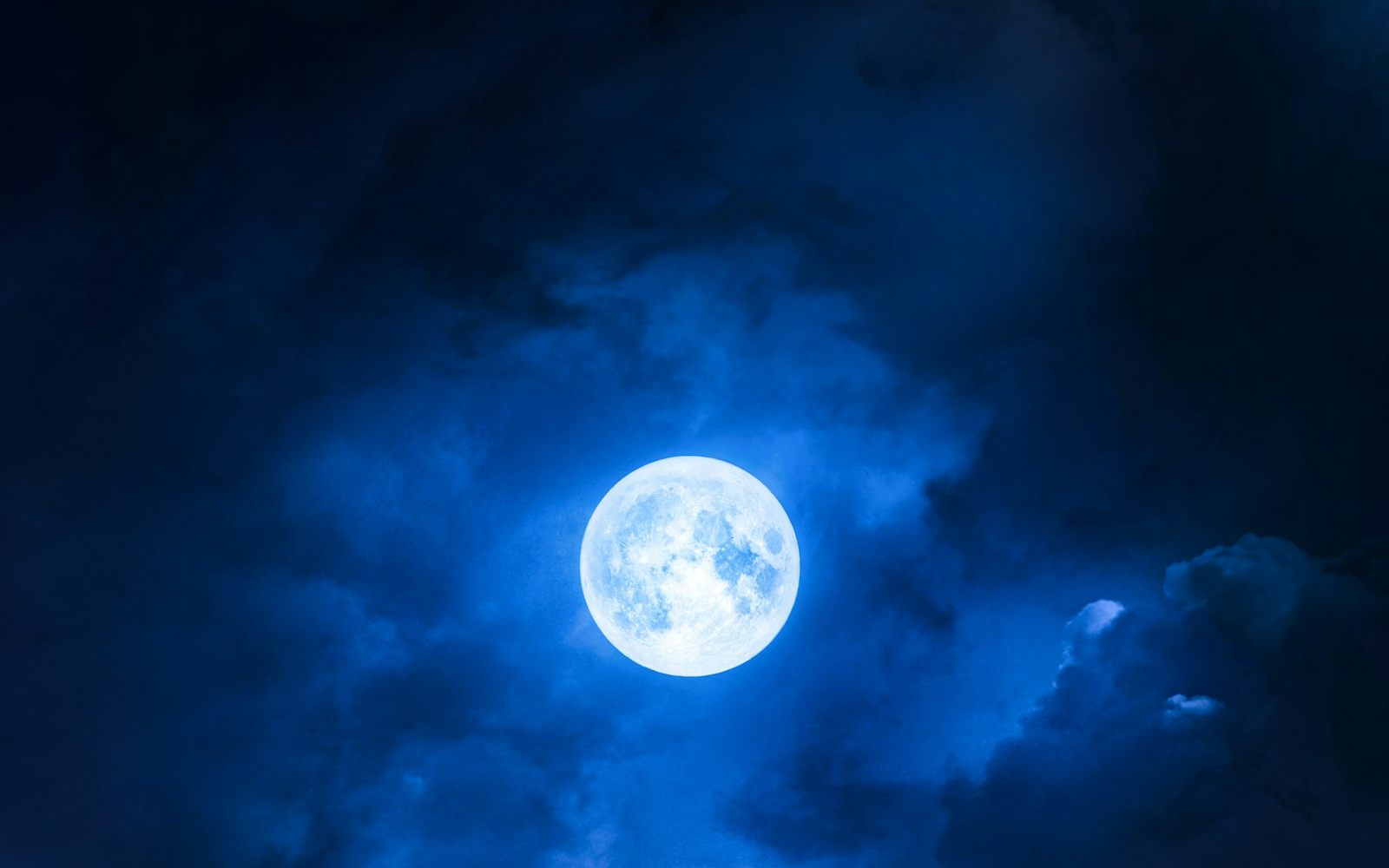 A bright full moon behind thin clouds in a dark blue night sky